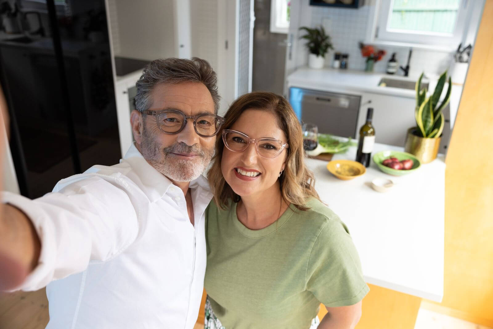 Two people standing in a kitchen, smiling at the camera wearing vital ready readers that are designed in new zealand.